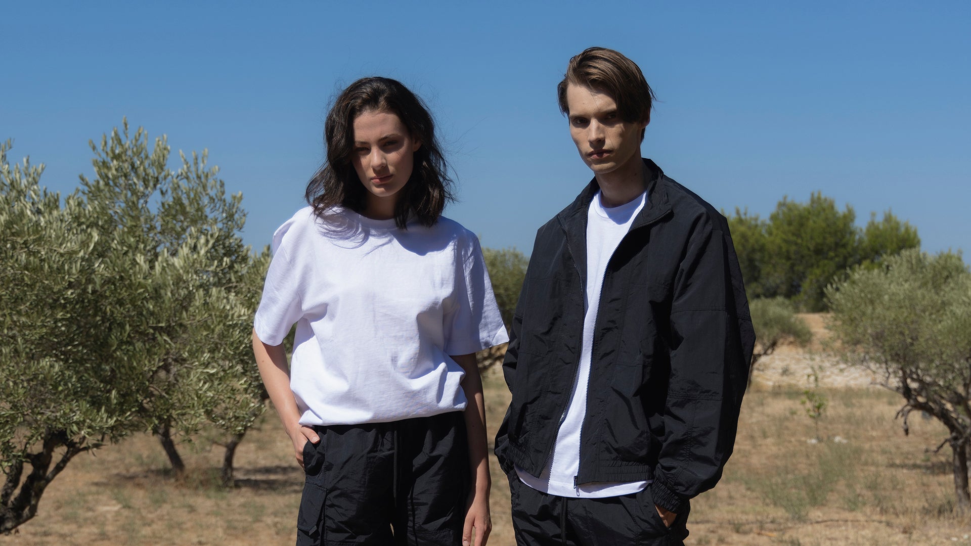 A  male model and a female model in cargo shorts and zipped-up jackets sit together on an outdoor staircase.