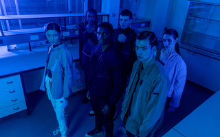Six models wearing cargo pants and jackets pose in a laboratory.