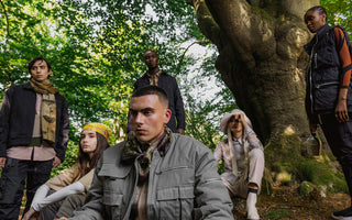 Six models wearing cargo pants and jackets pose in  a forest.